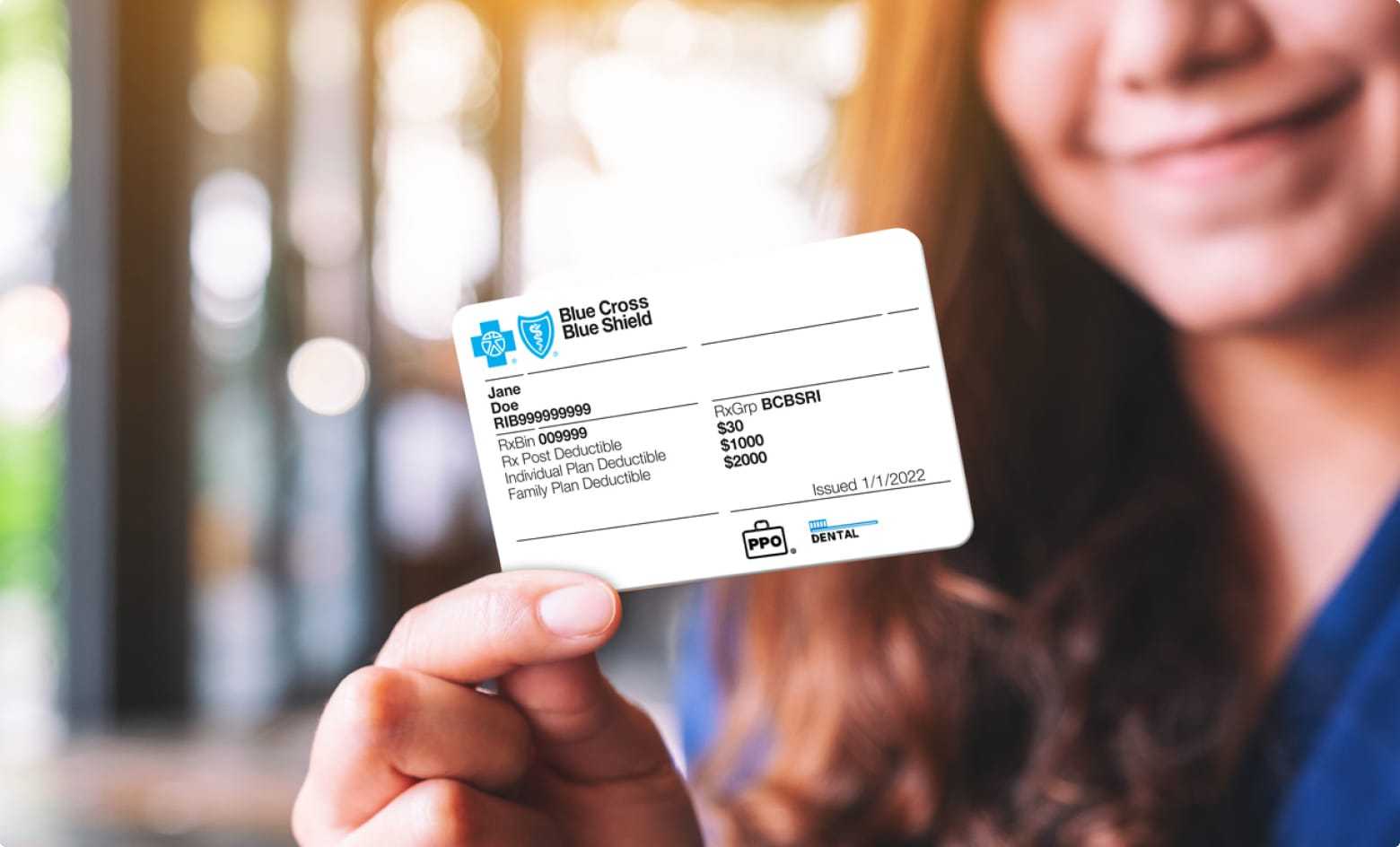 A woman holding a Blue Cross Blue Shield health insurance card.